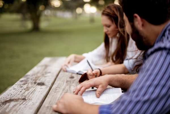 Closeup shot of people sitting in the park and reading the bible with a blurred background